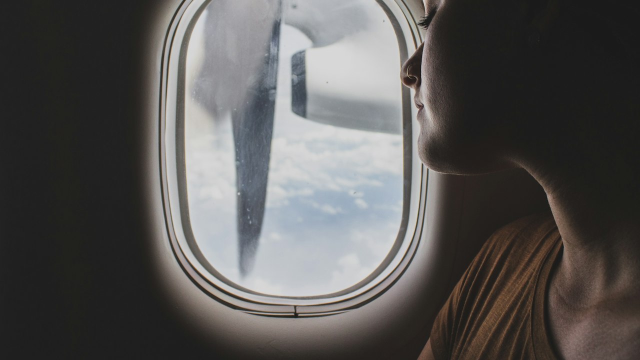 A traveller asleep by the airplane window, head resting against the seat back