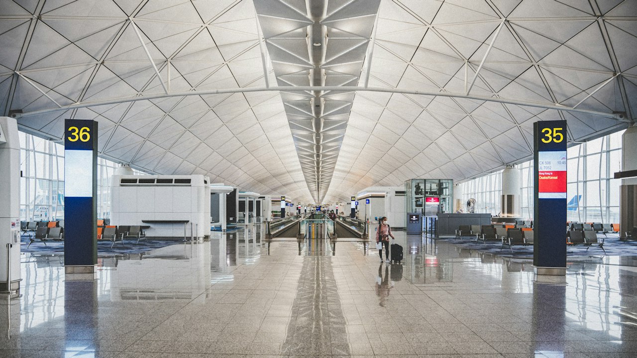 A wide airport terminal concourse with a polished floor and a diamond-pattern ceiling
